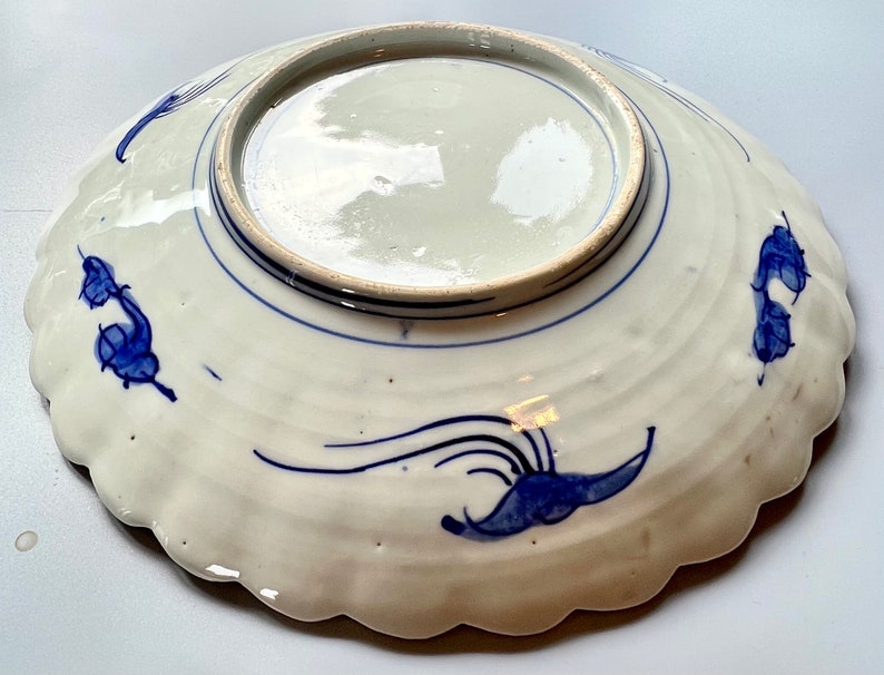 K&ouml;nnte beinhalten: Ein wei&szlig;er Teller aus Keramik mit einem blauen und wei&szlig;en Blumendesign. Der Teller hat einen gewellten Rand und ist mit einem blauen und wei&szlig;en Blumendesign verziert.