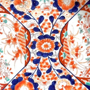 K&ouml;nnte beinhalten: Ein wei&szlig;er Teller aus Keramik mit einem gewellten Rand zeigt ein farbenfrohes Blumenmuster. Das Design umfasst blaue, orange und gr&uuml;ne Blumen und Bl&auml;tter. Der Teller ist ein dekoratives St&uuml;ck im traditionellen japanischen Stil.