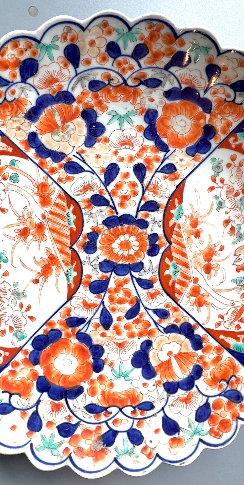K&ouml;nnte beinhalten: Ein wei&szlig;er Teller aus Keramik mit einem gewellten Rand zeigt ein farbenfrohes Blumenmuster. Das Design umfasst blaue, orange und gr&uuml;ne Blumen und Bl&auml;tter. Der Teller ist ein dekoratives St&uuml;ck im traditionellen japanischen Stil.