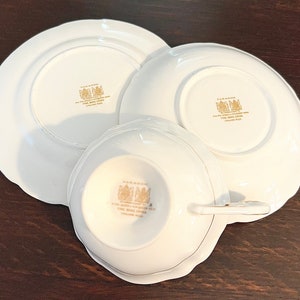 Puede incluir: Un juego de tres tazas de t&eacute; y platillos de porcelana blanca con ribetes dorados y las palabras "Paragon Fine Bone China England" en la parte inferior.