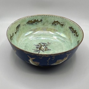 May include: A round ceramic bowl with a blue exterior and a light green interior. The bowl is decorated with fish and aquatic plant designs. The rim has a gold trim. The bowl's diameter is approximately 10 inches.