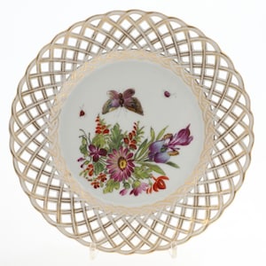 May include: A white porcelain plate with a gold lattice design around the edge. The center of the plate features a hand-painted floral design with a butterfly and insects.