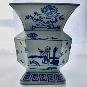 Puede incluir: Un jarr&oacute;n de porcelana azul y blanco con un dise&ntilde;o de drag&oacute;n y una figura. El jarr&oacute;n tiene una base cuadrada y una boca ancha.