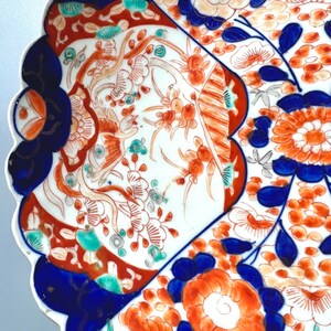 K&ouml;nnte beinhalten: Ein wei&szlig;er Teller aus Keramik mit einem gewellten Rand. Der Teller ist mit einem floralen Muster in Blau-, Rot- und Gr&uuml;nt&ouml;nen verziert. Die Blumen sind stilisiert und haben ein traditionelles japanisches Design.