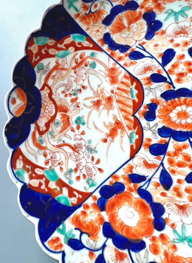 K&ouml;nnte beinhalten: Ein wei&szlig;er Teller aus Keramik mit einem gewellten Rand. Der Teller ist mit einem floralen Muster in Blau-, Rot- und Gr&uuml;nt&ouml;nen verziert. Die Blumen sind stilisiert und haben ein traditionelles japanisches Design.