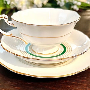 Puede incluir: Un juego de taza y platillo de t&eacute; blanco con borde dorado y c&iacute;rculos conc&eacute;ntricos verdes y dorados en el platillo.