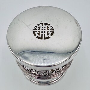 May include: Silver trinket box with a decorative, openwork lid featuring a circular design. The box has a silver, openwork base.