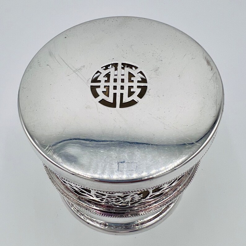May include: Silver trinket box with a decorative, openwork lid featuring a circular design. The box has a silver, openwork base.