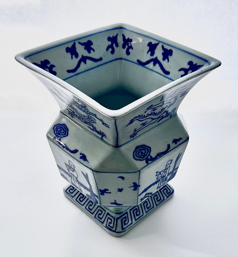 Puede incluir: Un jarr&oacute;n de porcelana azul y blanco con base cuadrada y dise&ntilde;o geom&eacute;trico. El jarr&oacute;n presenta un patr&oacute;n chino tradicional con figuras y &aacute;rboles.