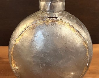 Könnte beinhalten: Eine silberne Metallvase mit rundem Korpus und einer strukturierten Oberseite. Die Vase hat eine Used-Look-Oberfläche mit goldenen Akzenten.