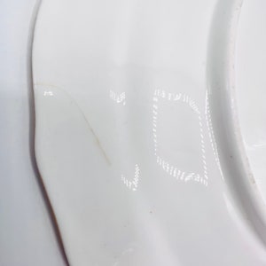 May include: Close-up of a white ceramic plate with a faint inscription of the letter "V" on the bottom.