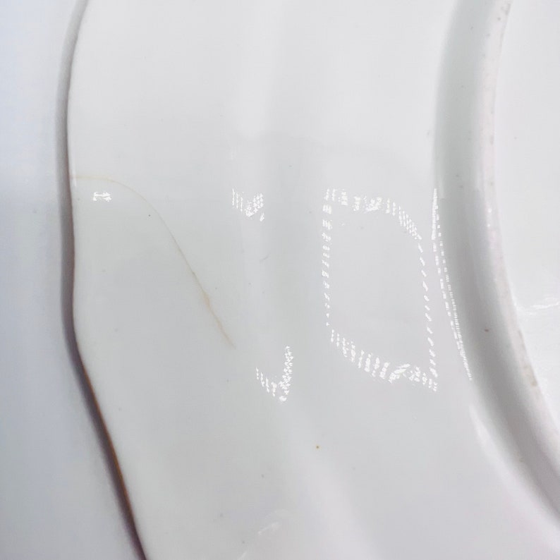 May include: Close-up of a white ceramic plate with a faint inscription of the letter "V" on the bottom.
