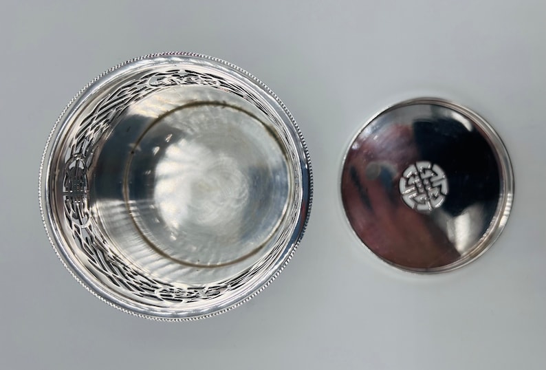 May include: Silver round box with a decorative design on the side and a lid with a Celtic knot design.