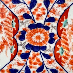 K&ouml;nnte beinhalten: Ein wei&szlig;er Keramikteller mit einem blauen und roten Blumenmuster. Die Blumen sind stilisiert und haben ein traditionelles japanisches Design. Der Teller ist mit goldenen Akzenten verziert.