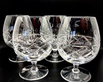 May include: Four clear glass brandy snifters with a cut crystal design. The glasses are arranged in a row on a black surface.