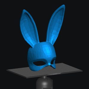 Puede incluir: Una máscara de conejo azul con orejas largas. La máscara tiene un diseño simple y está hecha de un material liso, similar al plástico.