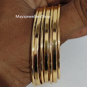 Puede incluir: Un conjunto de pulseras doradas. Las pulseras son lisas y brillantes, reflejando la luz. La imagen incluye el texto "MayajewellersShop".