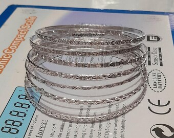 Pode incluir: Um conjunto de seis pulseiras de prata com designs intrincados. As pulseiras estão empilhadas umas sobre as outras e têm um acabamento brilhante.