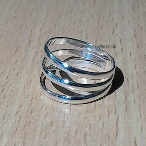 Puede incluir: Anillo de plata con cuatro bandas, cada banda es ligeramente más ancha que la de abajo. El anillo está hecho de plata pulida y tiene un acabado liso y brillante.  MayaJewellersShop está impreso en el anillo.