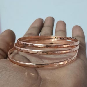 Op de afbeelding: Drie koperen armbanden op elkaar gestapeld. De armbanden zijn gehamerd en hebben een getextureerd oppervlak.