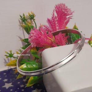 May include: A silver bangle bracelet with a smooth, polished finish. The bracelet has a slightly rounded edge and a subtle, textured design.