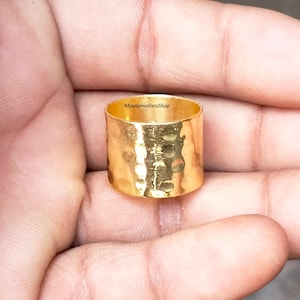 May include: A gold hammered ring with a wide band. The ring is made of metal and has a textured surface.