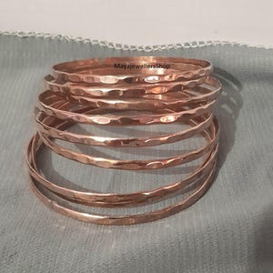 May include: A set of seven hammered copper bangles. The bangles are stacked on top of each other and are all the same size. The bangles are a warm copper color.
