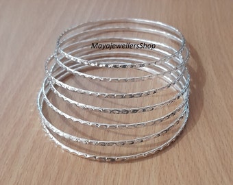 Peut inclure: Un ensemble de sept bracelets en argent avec une finition texturée martelée. Les bracelets sont empilés les uns sur les autres, créant un look superposé.