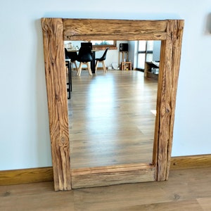 May include: A rustic wooden mirror with a rectangular frame. The frame is made of reclaimed wood with a natural brown finish. The mirror is reflecting a room with wooden floors and furniture.