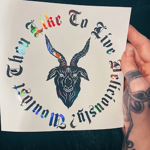 May include: A square decal featuring a black goat head illustration with a cross symbol on its forehead. The text 'Wouldst Thou Like To Live Deliciously?' is written in a circular gothic font with a holographic, multi-colored reflective finish.