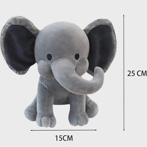 May include: A gray plush elephant toy with large ears, dark eyes, and a curved trunk. The toy is shown with dimension lines indicating a height of 25 cm and a width of 15 cm, which is approximately 9.84 inches in height and 5.91 inches in width.