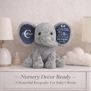May include: A grey plush elephant toy with large ears. The left ear features a white letter C and the name Callum. The right ear displays the date 11.03.2026, the weight 7 lbs 8 oz, and the time 04:34pm with small heart icons and baby footprints.