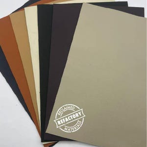 May include: A stack of eight different coloured leather sheets. The top sheet is a light beige colour. The sheets are arranged in a fan shape. The bottom sheet is a dark blue colour. The sheets are labelled "RECLAIMED REFACTORY MATERIALS".