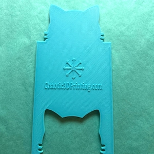 May include: A turquoise blue 3D printed cat-shaped phone stand with a snowflake design and the text "Chaotic3DPrinting.com".