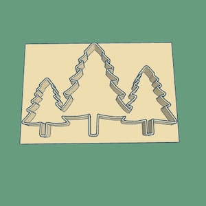 May include: A cookie cutter in the shape of three pine trees. The trees are outlined in a light brown color against a beige background.