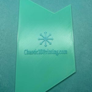 May include: A teal-colored, geometric-shaped object with a snowflake design and the text "Chaotics3DPrinting.com". The object has a textured surface and a unique, asymmetrical shape. The background is a matching teal color.