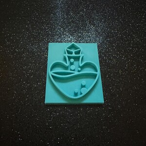 May include: A teal-colored rectangular silicone mold featuring a raised design of a heart-shaped potion bottle. The bottle has a stopper at the top and several small circular bubbles inside the heart shape, creating a clear, embossed outline.