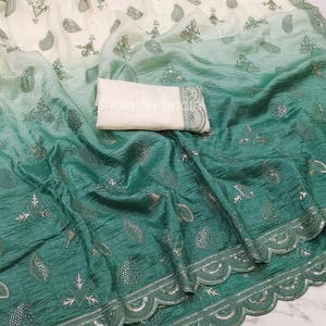 May include: A saree featuring an ombre transition from cream to deep green, adorned with embroidered paisley motifs and small sequins. The fabric has a crinkled texture, and the border is finished with a scalloped edge and silver embroidery.