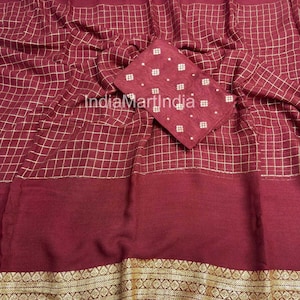 May include: A maroon fabric with a gold grid pattern and a matching maroon square piece with white and gold accents. The fabric has a gold border with an intricate design. The overall theme is a textile or garment.