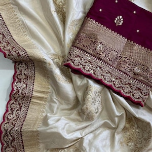 May include: Cream-coloured silk fabric with gold floral patterns and a deep burgundy border. The border features intricate gold embroidery and embellishments. A matching burgundy fabric with gold embroidery is also present.