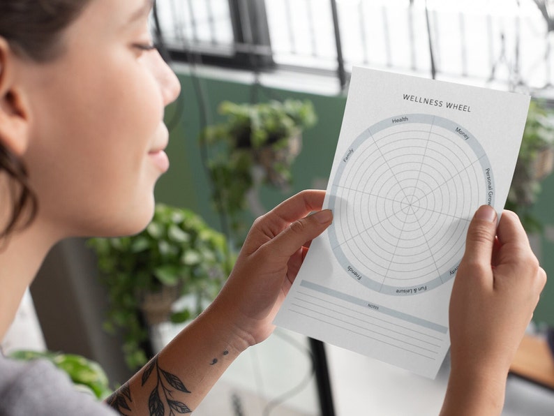May include: A person is holding a wellness wheel with categories like health, money, family, and personal growth. The wheel is printed on white paper with a light blue border.