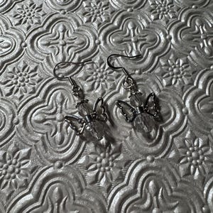 May include: A pair of silver butterfly earrings with clear crystal accents. The earrings are hanging from silver hooks.