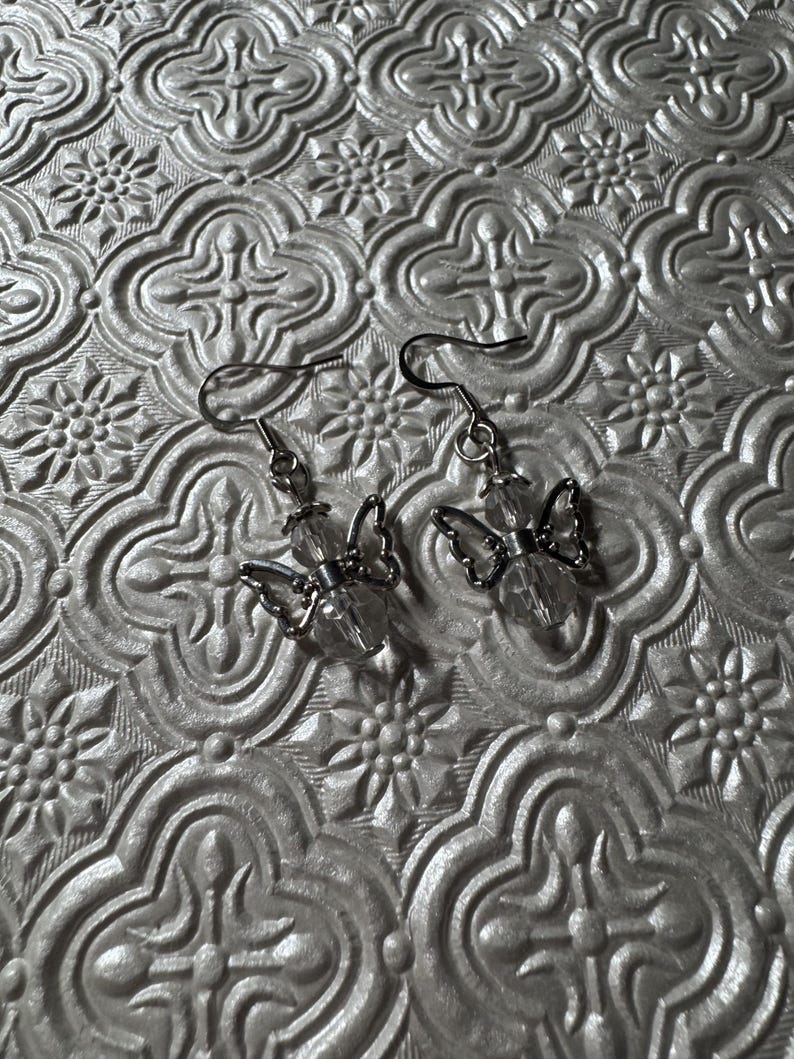 May include: A pair of silver butterfly earrings with clear crystal accents. The earrings are hanging from silver hooks.