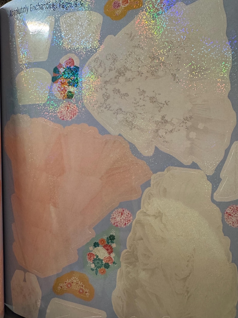 May include: A selection of iridescent stickers featuring diverse shapes and designs, such as floral arrangements, crowns, and abstract forms. The stickers have a shimmering, glittery effect and are set against a light blue backdrop. The text "Absolutely Enchanting: Pages 8-9" is visible.