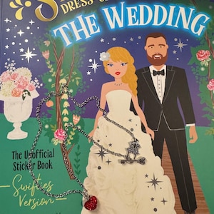 May include: A sticker book cover, "My Sticker Dress-Up Swifties: The Wedding", shows a bride and groom illustration. The cover text includes "Over 500 Reusable Shimmer Stickers." A silver necklace with a red heart pendant is in the foreground.