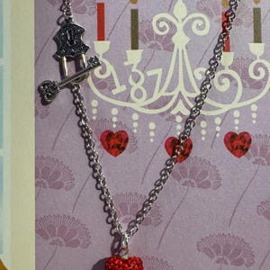 May include: A silver chain necklace with a red heart pendant. The necklace also features a key and lock charm. The background is a purple floral pattern with a chandelier and candles.
