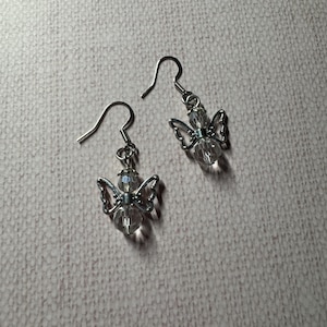 May include: A pair of silver dangle earrings with clear crystal angel charms.