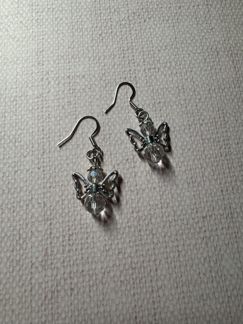 May include: A pair of silver dangle earrings with clear crystal angel charms.