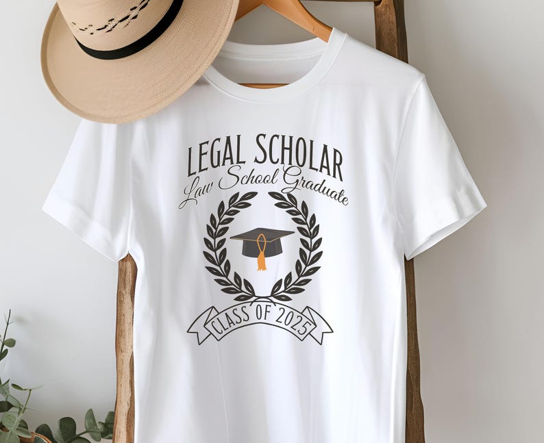 May include: White t-shirt with the text "LEGAL SCHOLAR Law School Graduate Class of 2025" and a black graduation cap with a gold tassel inside a laurel wreath.
