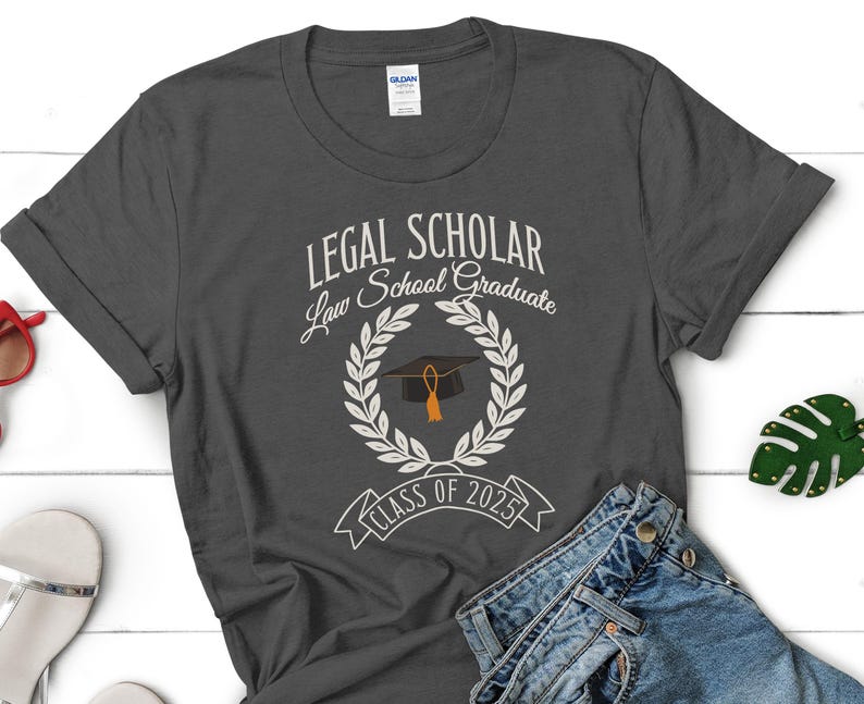 May include: A dark gray t-shirt with the text "LEGAL SCHOLAR Law School Graduate Class of 2025" and a graduation cap with a tassel in a wreath.